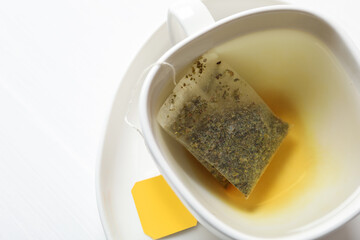 Tea bag in cup with water on white table, top view. Space for text