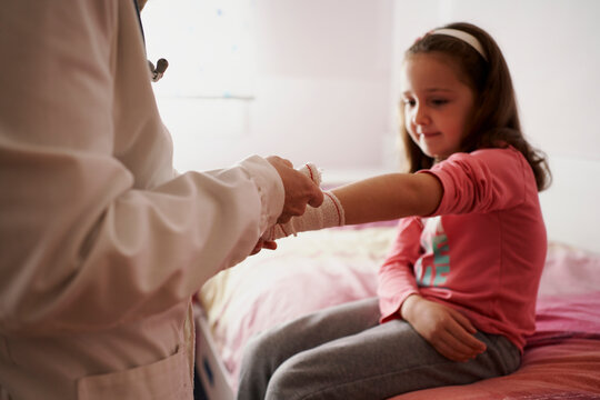 Female doctor bandaging the arm of a little girl in her room. Home doctor concept