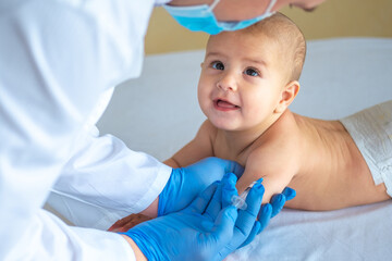 A doctor giving a vaccine to a baby in the hand. Happy child looks at the doctor