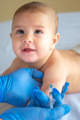 A doctor giving a vaccine to a baby in the hand. The child looks at the doctor and smiles. Vertical...