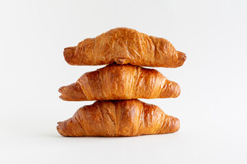 Three freshly baked croissants stacked on top of each other on a white background with copy space, horizontal