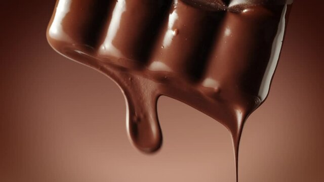 Melted chocolate dripping from a chocolate bar over a dark brown background, vertical camera movement. Chocolate dessert. Confectionery concept backdrop.