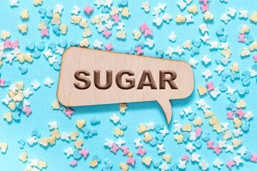 The word sugar is carved into a wooden callout or message on a blue background with sugar figurines. Medicine and health maintenance concept.