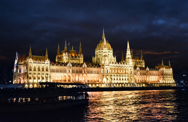 Fototapeta na wymiar Late night shot of the Budapest Parliament building illuminated as a tourist boat is seen in shadow in front in Budapest, Hungary.