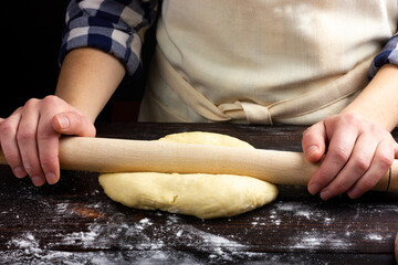 The process of rolling the dough with a rolling pin. Female hands roll out the dough. Woman baker rolls out the dough. Rustic style.