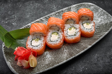 California sushi roll with cucumber avocado cream cheese and salmon on a gray plate on a dark background