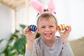 Fototapeta na wymiar Happy Easter kids. Boy in rabbit bunny ears on head with colored eggs at home. Cheerful crazy smiling child