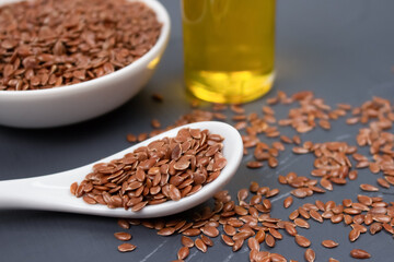 Flax seeds with a bottle of flaxseed oil behind on gray background - healthy eating or skin care concept. Top benefits of linseed in medicine and cosmetology. Selective focus