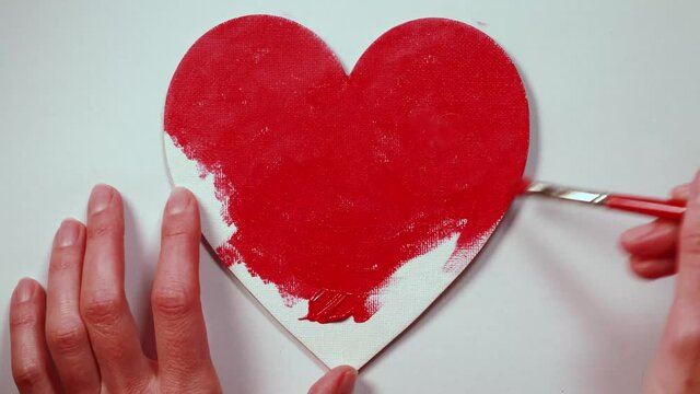 Top view of woman hands painting a heart-shaped canvas red on a white background. Timelapse video with a love concept.