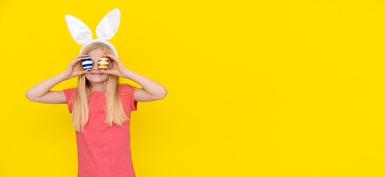 Happy Easter kids. Girl in rabbit bunny ears on head with colored eggs on yellow studio background Cheerful crazy smiling child. Banner copyspace.