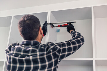 The carpenter sets the shelves in the kitchen in place with a clamp.