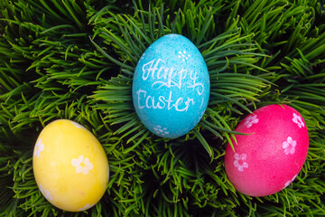 Three colored easter eggs on green grass. Top view