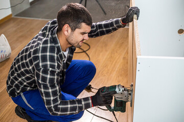 A carpenter with a corded jigsaw cutting a part of the wooden surface (board)