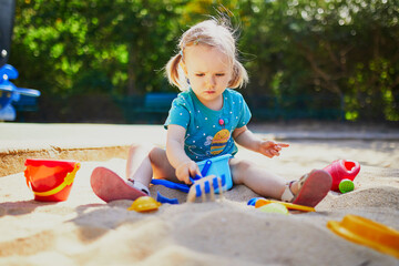 Adorable little girl having fun on playground in sandpit