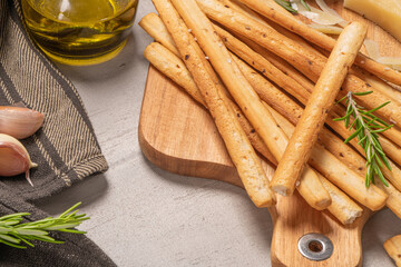 Traditional italian breadsticks grissini with rosemary, parmesan cheese, olive oil, garlic and salt on a gray background.