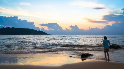 Fototapeta premium A woman is walking on the beach during the sunrise blue hours, travel and freedom concept, morning walk along the sea