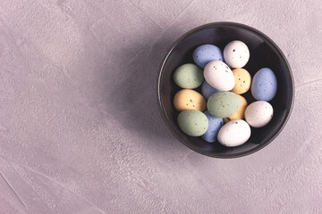 Candy Easter eggs in a dark ceramic bowl on gray concrete background. Top view, copy space for text. Holiday decoration concept.