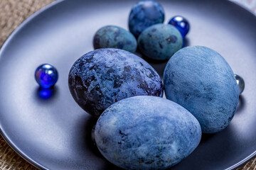 Blue Easter eggs on a dark ceramic plate on burlap on an light wooden background