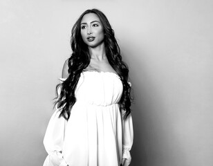 Beautiful young woman with long shiny black hair and natural make-up posing in dress on grey background 