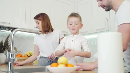 young family with small children in the modern white kitchen. Two little boys help their parents with cooking. Wash the fruit. Spend time together at home. Dad and mom have fun polite kids at home.