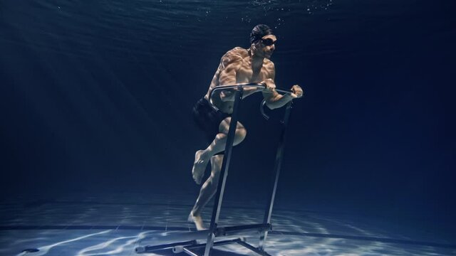 Cinematic shot of young male athlete with muscular body is exercising with effort and determination on stationary treadmill machine underwater. Concept of sport, fitness, healthy lifestyle, recreation