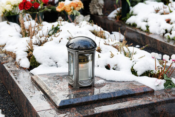 grave light on a snow covered grave with flowers in the background