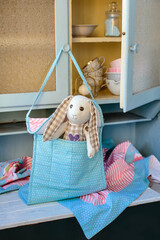 Shabby chic Easter composition with a vintage cabinet, dishes, tablecloth and handmade toy rabbit. Vertical image.