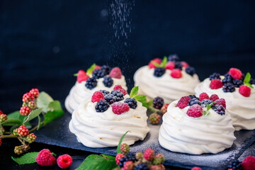 Homemade meringue basis for cake Pavlova with fresh blueberries and BlackBerry and powdered sugar on black concrete texture background. Copy space