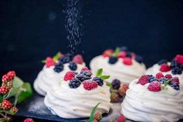 Homemade meringue basis for cake Pavlova with fresh blueberries and BlackBerry and powdered sugar on black concrete texture background. Copy space