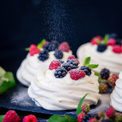 Homemade meringue basis for cake Pavlova with fresh blueberries and BlackBerry and powdered sugar on black concrete texture background. Copy space