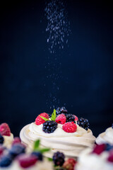 Homemade meringue basis for cake Pavlova with fresh blueberries and BlackBerry and powdered sugar on black concrete texture background. Copy space