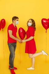 Medicine flu virus ill sick disease treatment concept. Young loving couple in protective face mask hold hands on yellow background with red heart-shaped balloons. Valentines day. Social distancing