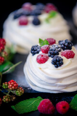 Homemade meringue basis for cake Pavlova with fresh blueberries and BlackBerry and powdered sugar on black concrete texture background. Copy space