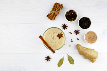 Fototapeta na wymiar A cup of masala tea. Ingredients for making spicy Indian masala chai. Dried black tea, milk, anise star seeds, cinnamon sticks,ginger, cardamom, black pepper and brown sugar.