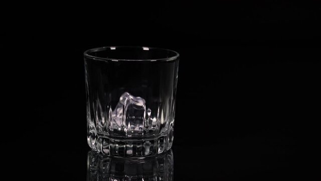 Single ice cup drops into empty glass in slow motion