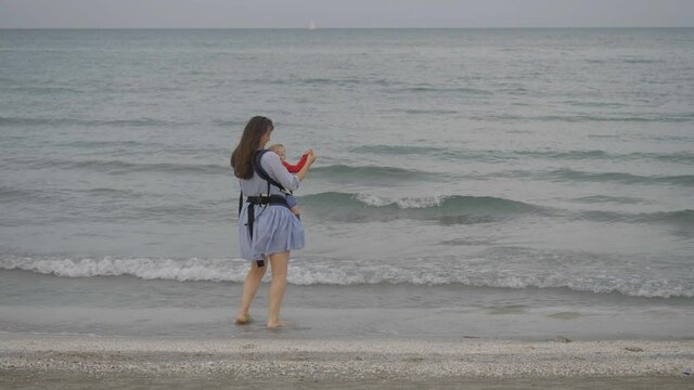 Mother carry baby  child in sling dace at seashore, maternity energy
