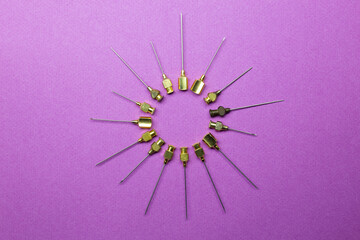 Obraz premium set of antique syringe needles of different sizes and thicknesses forming a circle in the shape of a coronavirus. Violet background