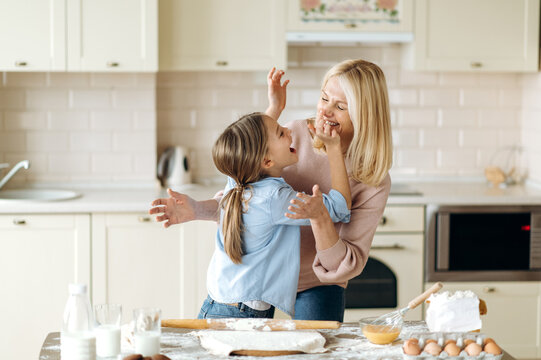 Caucasian happy mom or grandma and her beloved little daughter or granddaughter spend time together at the kitchen. Grandma teaches her granddaughter to cook pie, they are happy to cook together