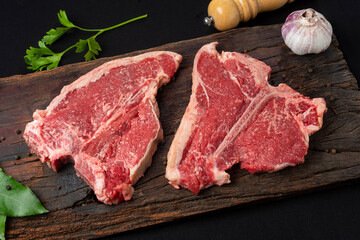 beef steaks on rustic board and metal plate with pepper shakers, garlic, spices, knife and grill...