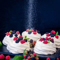 Homemade meringue basis for cake Pavlova with fresh blueberries and BlackBerry and powdered sugar on black concrete texture background. Copy space