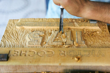 Manos de un hombre tallando con gubias sobre madera, trabajo artesanal 