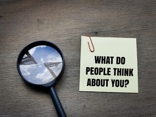 Selective focus side view text What do people think about you on sticky note with magnifying glass on wooden background.