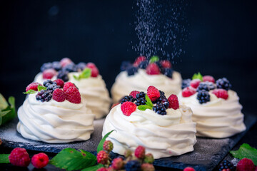Homemade meringue basis for cake Pavlova with fresh blueberries and BlackBerry and powdered sugar on black concrete texture background. Copy space