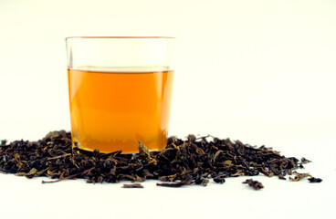 Hot golden, yellow tea in a clear white glass with dried tea leaves isolated on white background....