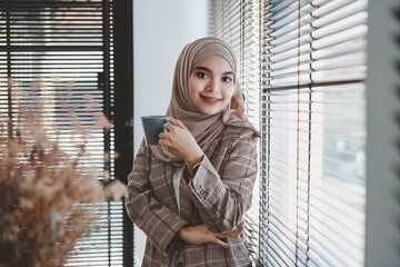 Confident asian muslim business woman brown hijab drinking coffee at modern office.