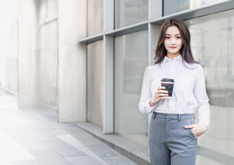 Fototapeta premium businesswoman holding a cup standing in front of the glass curtain wall