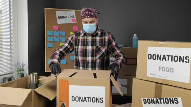 Volunteer in gloves and  face mask bring Donations box. Food Donation cardboard Box during the Covid-19 pandemic Coronavirus. 