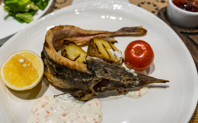 Half sturgeon in white caviar sauce with fried potatoes, tomato, and lemon
