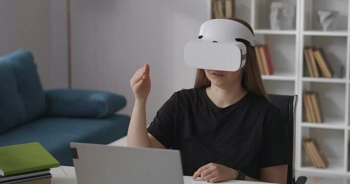 woman is wearing head-mounted display for viewing virtual reality, sitting at home, gesticulating by hand