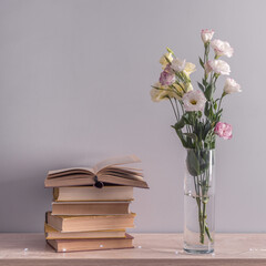 Eustoma flowers bouquet in a vase, stack of old vintage books and garland lights on a grey background. Reading and relax concept.